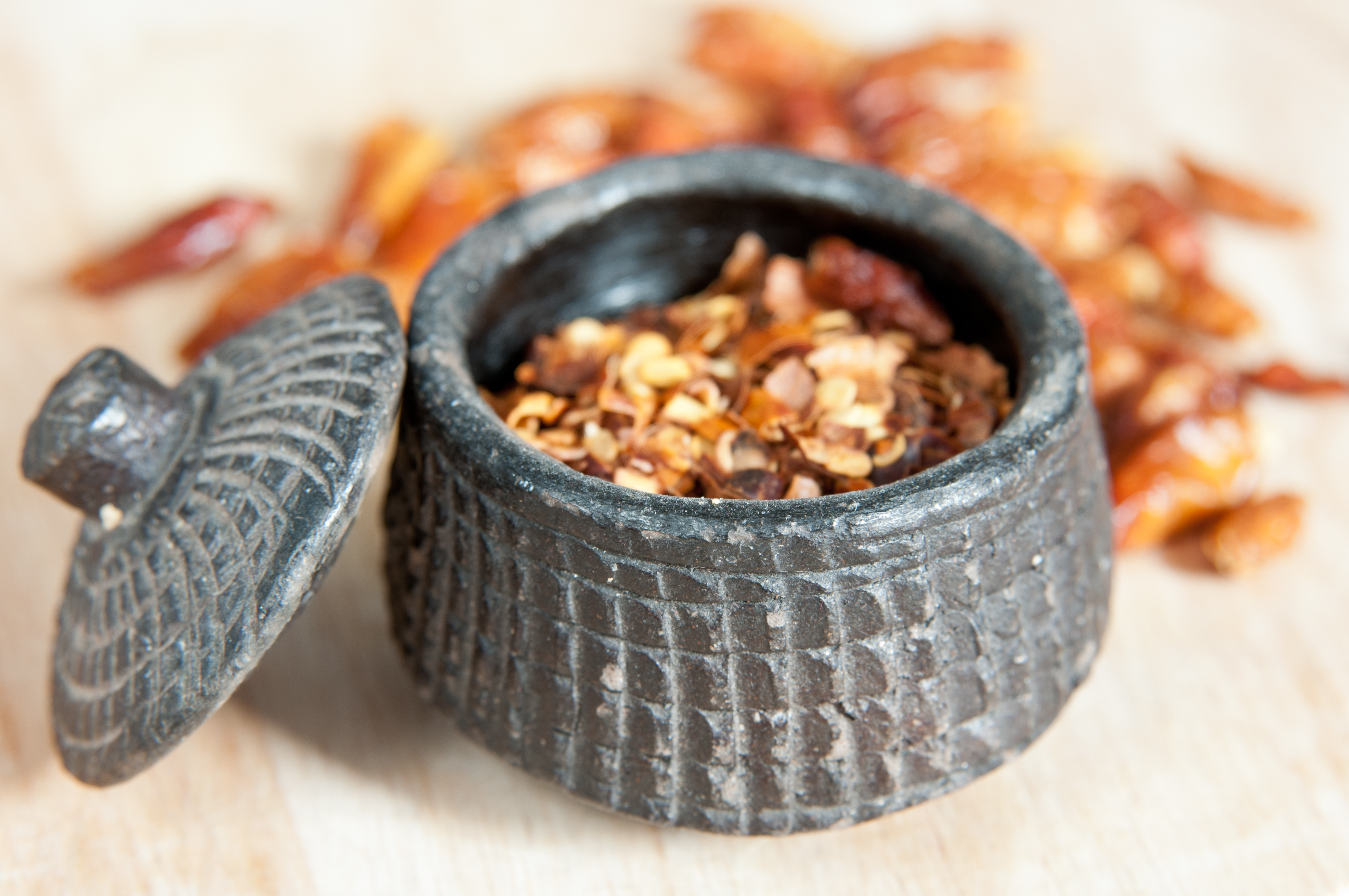 Red chili pepper crushed in a teracotta pot with whole chillies on background